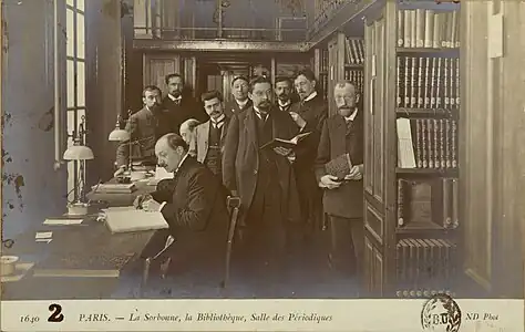 La salle des périodiques de la bibliothèque de la Sorbonne en 1905, de gauche à droite Ch. Beaulieux, Macaigne, Victor Mortet, Philibert de Clermont, M. Lévy, Bultingaire, F. Chambon, Borel et deux lecteurs assis à la table, Lucas de Peslouan et U. V. Chatelain (au fond).