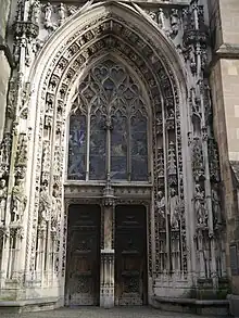  Grand Portail, ou portail de Montfalcon, entièrement restauré en 1892-1909. Porte principale à double battant avec trumeau à niche vide, créé à cette époque.