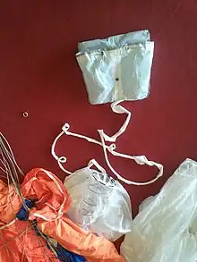 En haut, le POD de la voile de secours n'est pas solidaire de la voile de secours. L'extracteur de la voile de secours contient un ressort qui a pour but d'éloigner rapidement le POD du parachutiste afin qu'il soit dans le vent relatif et que la voile de secours s'ouvre vite et avec le moins d'interférence possible avec le parachutiste.