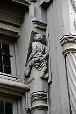 Photographie d'une sculpture sur bois, personnage montrant ses parties génitales, de dos, d'où son nom).