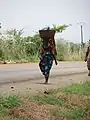 Femme marchant pieds nus, avec bébé au dos se rendant au marché sous un soleil ardent à Pobè au Bénin.