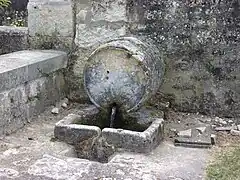 Photographie en couleurs d'une fontaine en pierre en forme de tonneau.