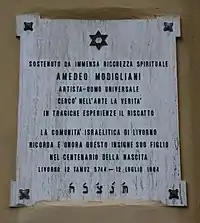 Photo en couleur d'une plaque carrée claire sur un mur avec des caractères noirs