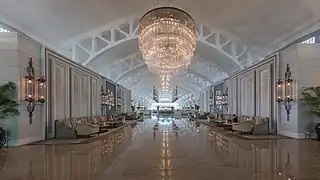 Vue symétrique du spacieux hall salon avec sofas et énorme luminaire se réfléchissant au sol, à l'hôtel The Fullerton Bay, Singapour. Juin 2018.