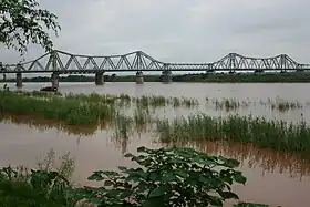 Vue éloignée d'un grand pont métallique passant au-dessus d'un fleuve.