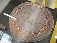 Photo : médaillon en métal en haut-relief d'un cœur rayonnant surmonté d'une croix et double tresse d'épines en bordure.