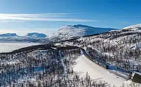 Malmbanan, tiré par une locomotive Bombardier IORE, entre Björkliden et Kopparåsen, un poteau d'arrêt ferroviaire. Vers la gauche la vallée Lapporten. Mars 2023.
