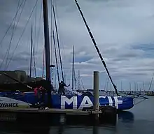 Vu de profil, avant d'un voilier bleu et blanc amarré au ponton.