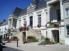 Photographie en couleur d'un bâtiment municipal et de son parvis longés par une voie publique.