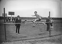 Photographie en noir et blanc d'une athlète féminine sautant au-dessus d'une barre.