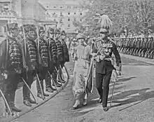 Une femme en grande tenue et un homme en uniforme de l'armée marchent dans une rue entourée de soldats.