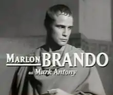Photographie en noir et blanc d'un homme portant la toge, le regard pensif vers la bas de l'image. Des caractères de grande taille, en surimpression, indiquent que Marlon Brando joue le rôle de Marc Antoine.