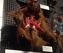 Masque du dieu Toshidon. Il possède une peau rouge, un long nez pointu et de longs crocs.