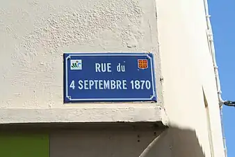 Nom de rue inscrit en blanc sur une plaque à fond bleu entouré de vert.