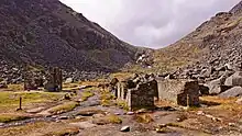 Photographie couleur des vestiges d'un village de mineurs près de Glendalough avec un ruisseau serpentant entre les anciennes bâtisses et des éboulis, avec une végétation très pauvre