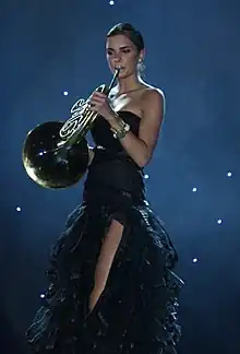 Une fille debout en robe sans bretelles joue du cor d'harmonie.