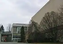 Une entrée de bâtiment à gauche et des arbres devant un mur.