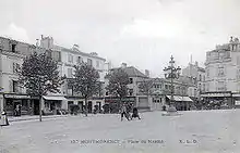 Carte postale noir et blanc : des enfants posent au centre ; autour, des maisons ; à droite, une calèche tirée par des chevaux.