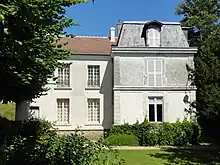 Maison ancienne de deux étages, aux murs blanc, entourée d'arbres.