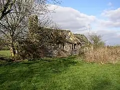 Photo d'un petit bâtiment en mauvais état, au toit percé et aux fenêtres béantes, à moitié dissimulé par un arbre