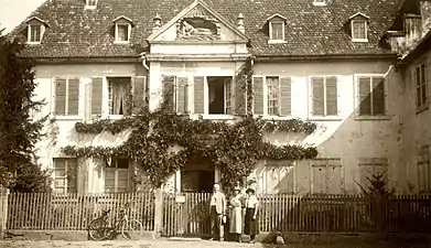 Photographie noir et blanc d'un bâtiment classique précédé d'un jardin grillagé.