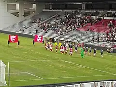 Photographie en couleur d'un terrain de football où deux équipes font leur entrée.