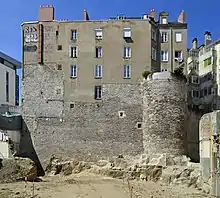 Façade d'un bâtiment ancien, dont le soubassement est un haut mur et une tour de pierre