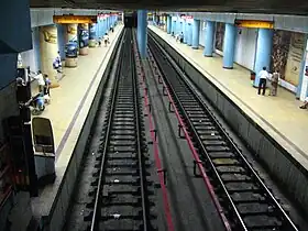 au centre les deux voies encadrées par deux quai latéraux avec des poteaux de soutien ronds et peints en bleu.