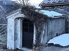 Photographie d'un oratoire en hiver qui a de la neige sur son toit, on voit sa porte en bois.
