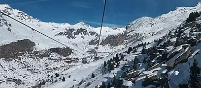 Photographie d'une cabine devant un paysage enneigé, formant un vallon entre les montagnes où se trouvent des remontées mécaniques.