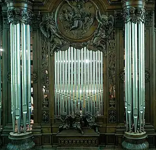 Plate-face d'un grand buffet d'orgue en bois, avec trois statues d'angelots musiciens au bas de l'image, deux tourelles à droite et à gauche et, en haut de l'image, un médaillon d'un homme entouré d'anges.