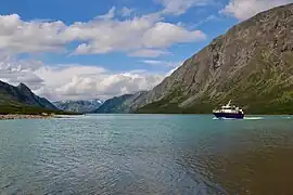 Petit bateau sur un grand lac turquoise cerné de montagnes.