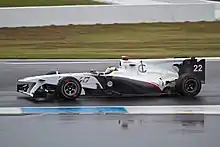 Photographie d'une monoplace blanche, vue de profil, sur une piste humide.