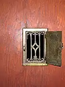 Une ouverture avec une grille de laiton ouvragée et un volet opaque