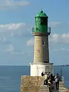 Vue d’un phare au bout d’une jetée, corps en granit et lanterne verte.