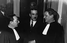 Dans un couloir du Palais de Justice, Bonny, souriant, plaisante avec ses deux avocats.