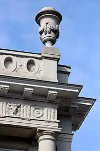 Coin de l'avant-corps surmonté d'une frise, d'un attique et d'un vase.