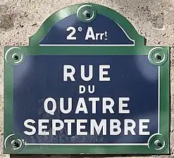 Nom de rue inscrit en blanc sur une plaque à fond bleu entouré de vert.