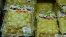 Photo de sacs de pommes de terre régulièrement empilés ; l’emballage transparent de chacun porte en grand, directement imprimé sur le plastique, la mention « Pommes de terre cuites à la vapeur » et, dans le bas, celle des ingrédients (pommes de terre, anti-oxygène, disulfite de sodium), des conseils de conservation et de préparation (à froid, au micro-ondes, à la poêle), des informations nutritionnelles et de recyclage, un numéro d’appel téléphonique ; une étiquette collée sur le sachet donne la date de péremption et un code.