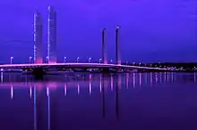 Photographie du pont Jacques Chaban-Delmas de nuit. La nuit est éclairée par le pont, qui reflète des couleurs violettes dans l'eau de la Garonne.