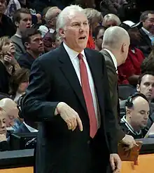 Gregg Popovich en costume, un adjoint dans son dos.