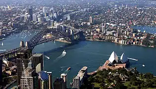 Vue aérienne du port de Sydney, avec l'opéra (qui s'avance comme un promontoire sur l'eau) et le pont.