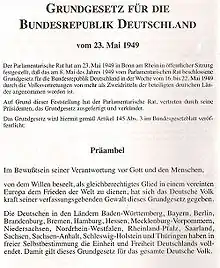 Première page du texte de la loi fondamentale de la république fédérale d'Allemagne, en allemand. En haut de la page, centré et en gras, l'intitulé : Loi fondamentale de la république fédérale allemande du 23 mai 1949. Après 9 lignes de texte dactylographié, centrées et dans une police non accentuée, le titre Préambule, centré et en gras, se trouve au milieu de l'image ; suivent les premiers paragraphes du texte du préambule, dans une police non accentuée.