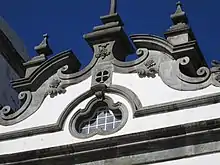 Photographie en couleurs. Gros plan sur le fronton blanc au relief couleur de pierre.