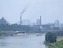 Photographie d'une usine dégageant de la fumée sur le bord d'une rivière.