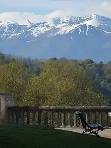 Photographie en couleurs d'un paysage de montagnes enneigées en arrière-plan d'une vallée boisée.