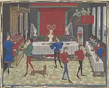 Enluminure médiévale représentant un banquet. Les serviteurs portent de longues chaussures. Deux des dames attablées sont coiffées d'un hennin.