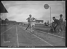 Photographie en noir et blanc d'un homme en tenue foncée de l'équipe de France portant le dossard no 22. Il s'agit de René Wiriath. Il devance un homme en tenue blanche, représentant l'équipe d'Allemagne, portant le dossard no 15
