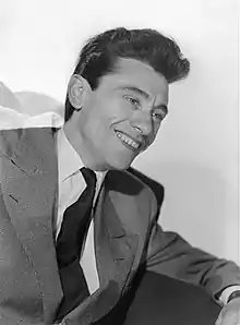 Portrait photo noir et blanc d'un jeune homme très souriant, posant en costume de ville.