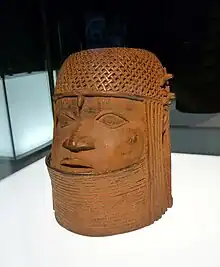 forme cylindrique en laiton représentant un visage humain avec une coiffe tressée